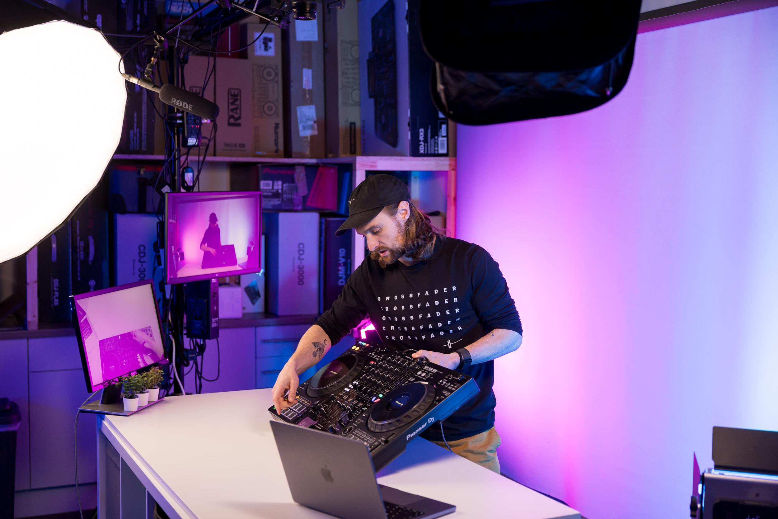 Crossfader DJ tutor working at the decks with a record library backdrop.